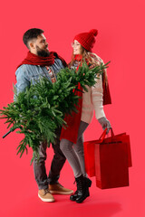 Young couple with Christmas tree and shopping bags on red background