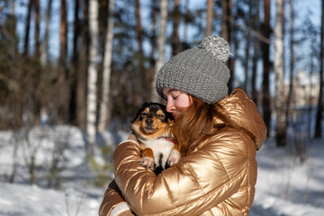 A young girl in the forest in winter holds a dog in her arms and enjoys the weather and the sun outdoors