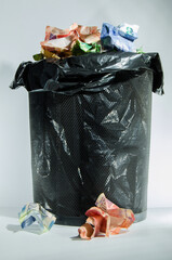 Trash bin filled with South-African rand notes in black bag