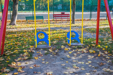 Children's swing on the playground. Yellow leaves in the playground. Gold autumn. Yellow leaves are scattered on the playground on a sunny day
