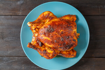 Whole baked chicken carcass with a crust on a blue plate on a wooden table.