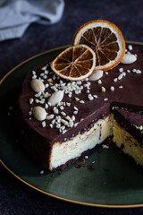 Ukrainian cheesecake syrnyk with chocolate and almond glaze on green plate on dark background .