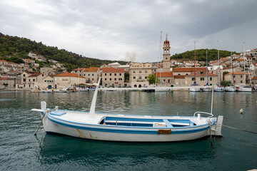 Beautiful blue and white fishing boat in front of Pucisca church, Croatia with wildfire smoke visible in the distance