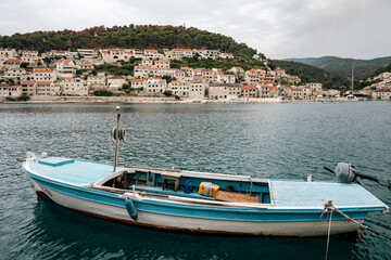 Fototapeta premium Beautiful blue and white fishing boat in front of Pucisca church, Croatia with wildfire smoke visible in the distance