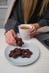 A woman with a cup of tea sits at a table with a sweet cookie in her hands. Delicious traditional desserts
