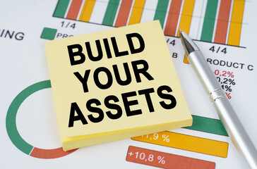 On the business charts are a pen and stickers with the inscription - Build Your Assets