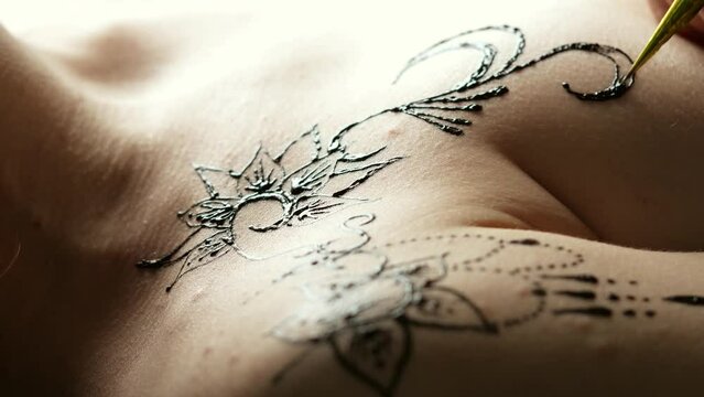 Artist applying henna tattoo on bare woman chest
