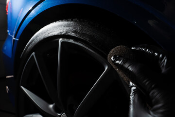 Tire blackening process. Auto detailing service worker applies rubber blackening agent in garage.