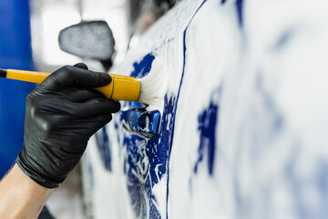 Fototapeta na wymiar Hand brush washing of car body with foam in car detailing service. Car wash worker washes a car body.