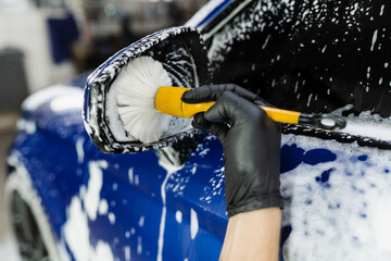 Hand brush washing of car side mirror with foam in car detailing service. Car wash worker washes...