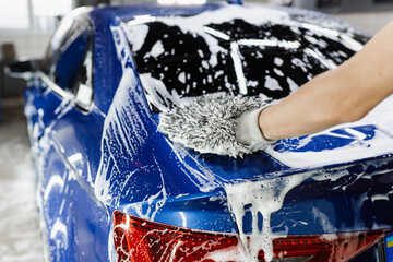 Car washer doing manual foam washing in auto detailing service. Hand washing with microfiber glove...