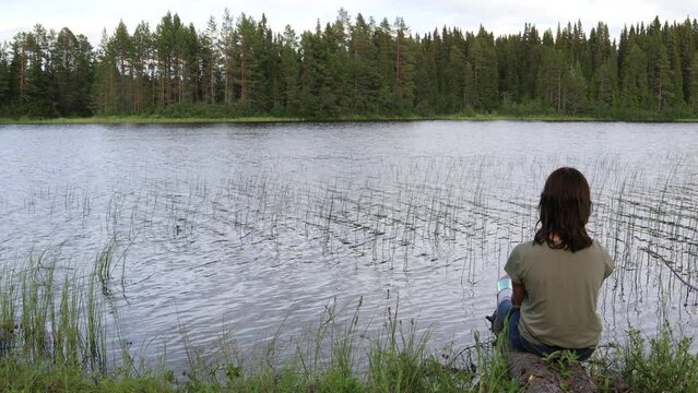 Girl sitting at a lake. Great view. Cloudy summer day. J&auml;mtland, Sweden, Scandinavia, Europe.