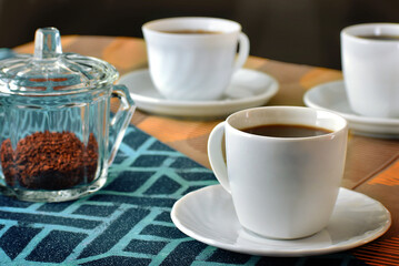 table with three cups of black coffee on a dark background. Orange and blue tablecloth