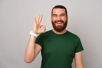 Fototapeta premium Photo of joyful young bearded man showing OK gesture over grey backdrop