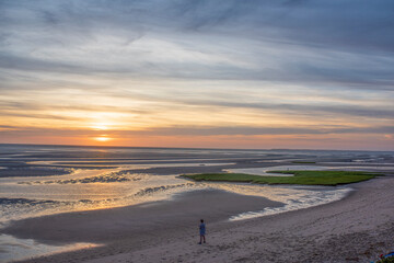 A man looks out at the sunset during low tide