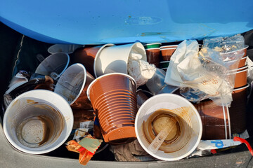 Trash bin full of discarded used coffee cups and plastic packaging, recycling waste concept