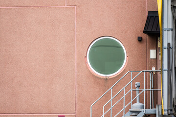 Round window on a pink concrete industrial building.