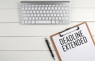 Home office workspace with keyboard, clipboard and pen with text DEADLINE EXTENDED on white wooden background , business concept