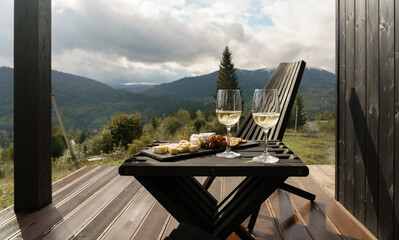 White wine glasses and plate of cheese on terrace with mountains view