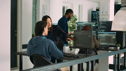 Obraz premium Asian team of artificial intelligence cloud programers talking about programming in it agency office. Compiling code on terminal window server, doing teamwork on developing algorithms.