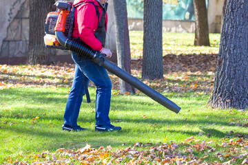 Leaf blower Male worker removes leaves lawn of garden autumn. Removing fallen leaves in autumn....