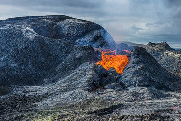 Landscape in Iceland on the Reykjanes Peninsula. low lava flow from an active volcanic crater. Crater with cooled and liquid magma rock. dark magma around the crater with little steam and smoke