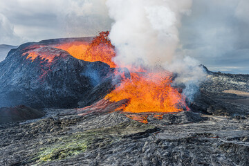 active volcano on Iceland. glowing hot lava with fountain from the volcanic crater on Reykjanes Peninsula. Landscape in Geopark in daylight. strong development of steam over the volcanic crater