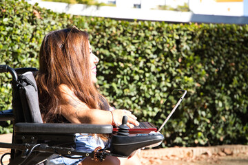 young disabled woman in wheelchair and reduced mobility with her laptop computer teleworking in the...