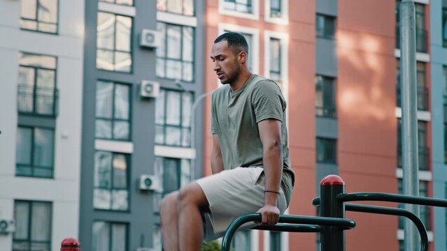 Latina sportsman athletic muscular african man on city sport ground training press abs muscles by lifting legs with bended knees on parallel bars healthy male athlete performing bodybuilding exercises