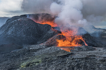 Volcano on Iceland after eruption. Hot steam clouds over crater opening. Lava flows from the volcanic crater. Landscape on Reykjanes peninsula at day. dark magma rock in the foreground - obrazy, fototapety, plakaty