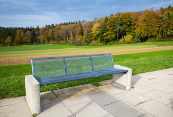 A blue metal bench on a viewing platform at the edge of the autumn forest above Embrach, Switzerland