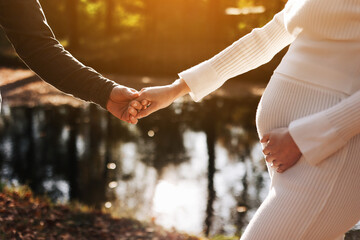 cropped photo of couple, man and pregnant wife are holding hands and walking by the lake on...