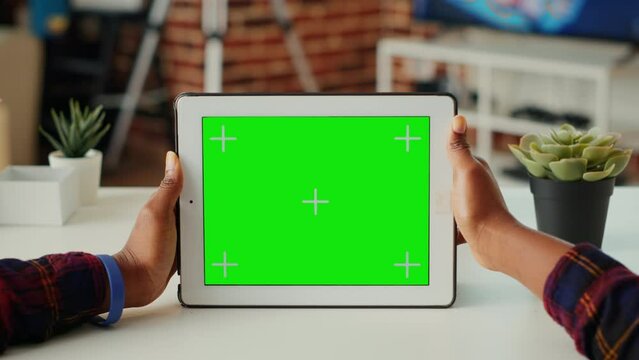 Young adult holding digital gadget with horizontal green screen, looking at blank background on modern device. Analyzing isolated chroma key display and mock up template. Close up.