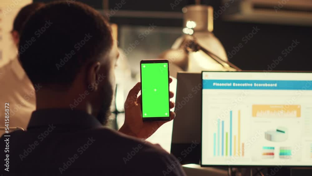 Poster startup employee holding smartphone with greenscreen and working on company data, looking at isolate