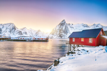 Traditionelle norwegische rote Holzhäuser (Rorbuer) am Ufer des Reinefjorden in der Nähe des Dorfes Hamnoy bei Sonnenuntergang.