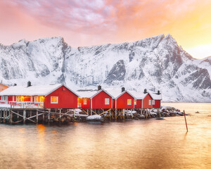 Fototapeta premium Traditional Norwegian red wooden houses (rorbuer) on the shore of Reinefjorden near Hamnoy village at sunset.