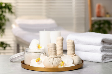 Fototapeta na wymiar Tray with herbal bags, candles, scrub, beautiful flowers and folded towels on grey marble table in salon, space for text. Spa products
