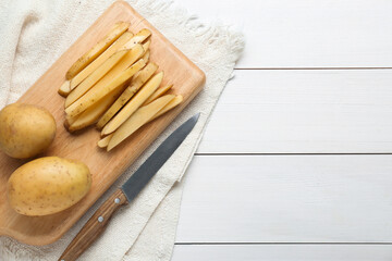 Potatoes and knife on white wooden table, top view with space for text. Cooking delicious french fries