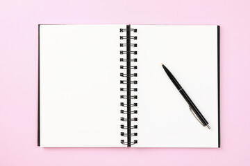 Notebook and pen on pale pink background, top view