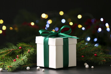 Christmas present. Beautiful gift box and fir tree branches on black table against blurred festive...