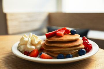 Tasty pancakes with fresh berries and whipped cream on wooden table
