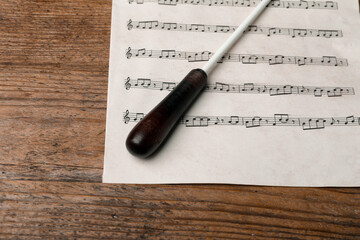Conductor's baton and sheet music on wooden table, above view