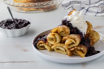 A pile of freshly made crepes topped with blueberry sauce and whip cream.