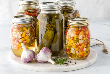 Jars of pickles and pickled peppers on a marble slab against a light background.