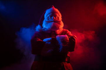 Santa Claus stands with his arms crossed on his chest in blue red neon light and smoke. 