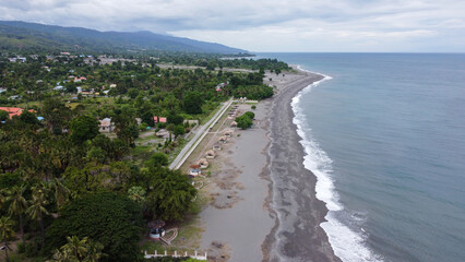 Fototapeta na wymiar Aerial drone landscape view of black sandy beach, ocean waves and tree covered terrain in town of Liquica, Timor Leste, Southeast Asia