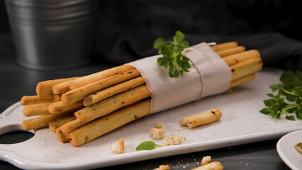 Fresh baked homemade grissini bread sticks in white ceramic tray with olive oil and basil herbs...