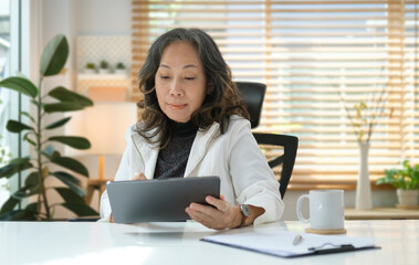 Happy senior woman surfing internet, checking email on digital tablet..