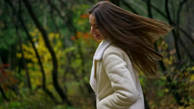 Cheerful happy long-haired lady having fun in the autumn park. Lady in white jacket turns in front of camera showing her beautiful hair.