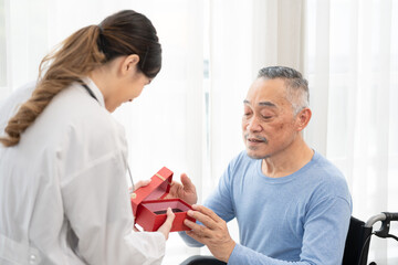 senior man receives a gift box from asian female doctor for happy birthday.